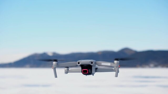 in the frame from the bottom up, a drone appears against the background of mountains in winter, slowly rises up, turns around and flies away. aerial monitoring from a height. slow motion. close-up.