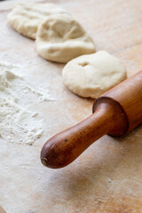 A rolling pin, raw dough and flour lie on a wooden table. The dough is being prepared for baking.