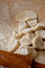 A rolling pin, raw dough and flour lie on a wooden table. The dough is being prepared for baking.