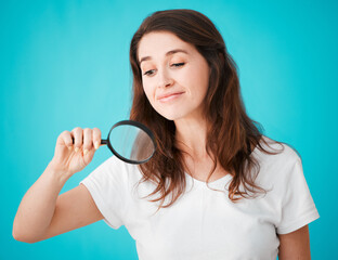 Shes on the case. Studio shot of an attractive young woman posing with a magnifying glass against a blue background.