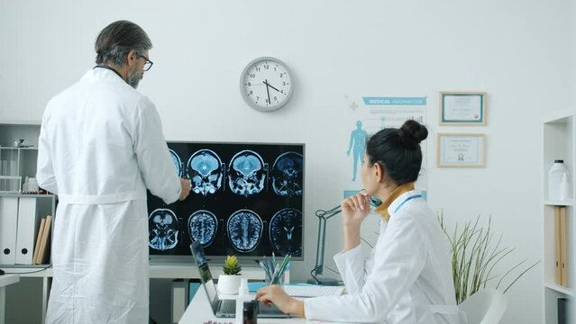 Doctors male and female wearing white coats analyzing brain scans and discussing disease in hospital room. Medicine and healthcare concept.