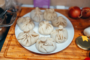 Raw khinkali is being prepared for cooking. A plate full of hinkals. Wooden cutting board, white plate. Meat and dough. Beautiful khinkali. Kitchen.
