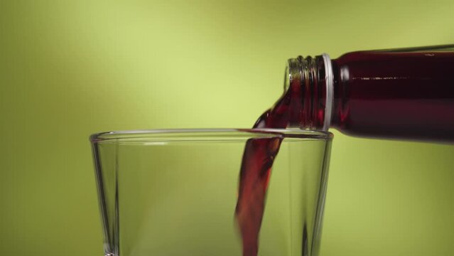 Cherry juice drink pouring in glasses on green colorful background. Close up healthy beverage for detoxification. Bubbles appear. Vitamins, fruits. 