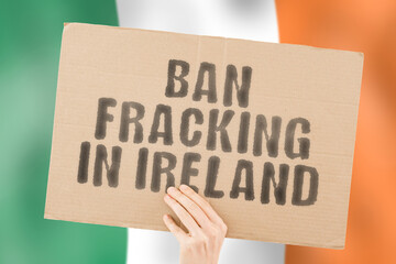 The phrase " Ban fracking in ireland " is on a banner in men's hands with a blurred Irish flag in the background. Pipeline. Resource. Money. Politics. Pollution. Profit. Petrol. Pumping. Crude