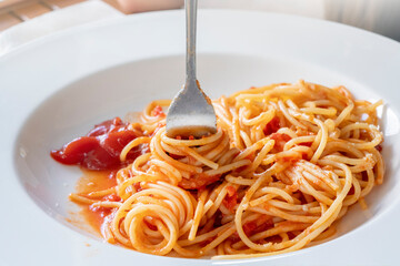 A white plate with spaghetti and a fork with twisted durum wheat pasta . lunch close-up outdoor with tomato sauce ketchup