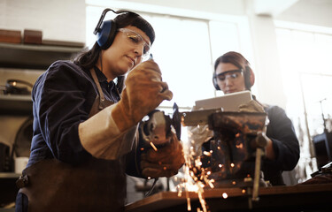 Its gotta be perfect. Cropped shot of two attractive young female artisans using an angle grinder in their workshop.