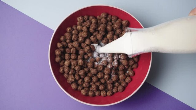 Milk pouring into sweetened rice cereal from glass into red bowl of with splashing in slow motion. Coco Pops, Rice Krispies that contains real chocolate. Cereal Breakfast for especially kids.