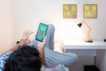 Young man lying in bed and paying for online shopping with PIX. Using mobile app to pay for orders via instant payment.