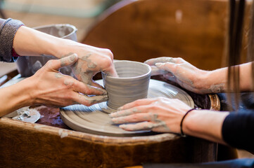 Fototapeta na wymiar Hands of two people create pot on potter wheel.