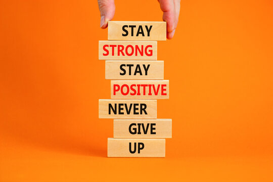 Never give up symbol. Wooden blocks with concept words Stay strong stay positive never give up. Beautiful orange background. Copy space. Businessman hand. Motivational business never give up concept.