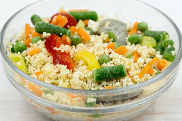 Frozen food: mix of couscous, vegetables and sauce in a glass bowl on a white table