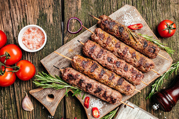 Lula kebab, traditional Caucasian dish. On the black background of the concrete, on a chopping board, with ketchup, spices and tomatoes copy space above