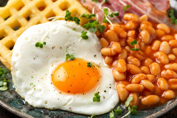 Potato waffles with fried egg, bacon and baked beans. Morning breakfast