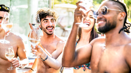 Trendy friends drinking white wine champagne at swimming pool party - Vacation life style concept with young guys and girls having fun together on summer day at luxury resort - Warm bright filter