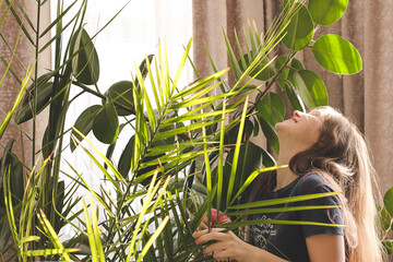 Young teenager girl watering plant in flower pots at home. Hobby and leisure, nature in the house. Indoor plants in pots, spraying watering nutrition fertilizers transplanting. Home garden concept.