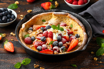 Dutch baby pancake with berries and icing sugar in a iron cast pan. Morning breakfast