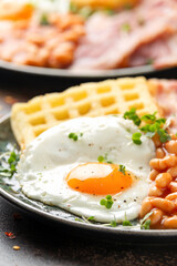 Potato waffles with fried egg, bacon and baked beans. Morning breakfast