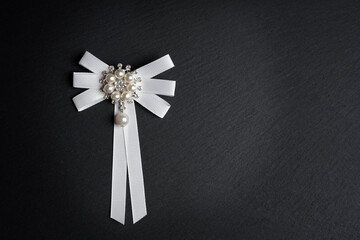 Bow decoration with a crooked pattern of sparkling pearls on a dark background - obrazy, fototapety, plakaty