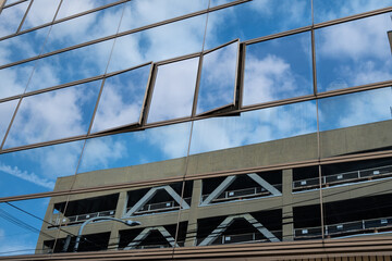 空と雲と駐車場が映ったガラス張りのビジネスビル