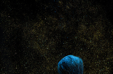 make-up brush with powder of different colors on a dark background like space dust