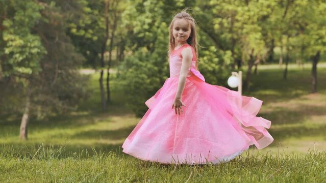 A girl in a pink princess dress is spinning in the park.