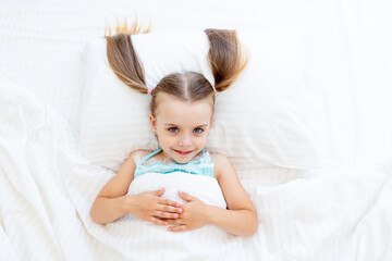 a baby girl is sleeping or has woken up in the morning on a bed at home on a white cotton bed and is smiling sweetly