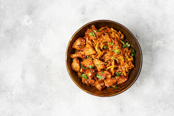 Udon noodles with chicken in teriyaki sauce in a brown bowl on a light gray culinary background. Top view from the copyspace