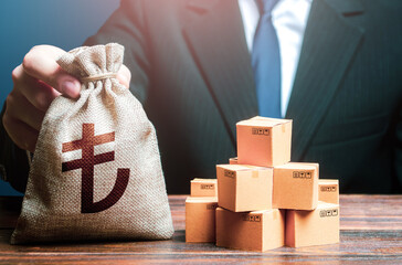 Businessman holds turkish lira money bag and boxes with goods. Business income. Payment of taxes...
