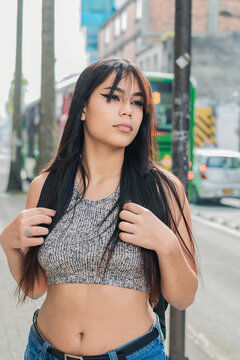 beautiful latina woman with brown skin, standing on the street while waiting for the bus to go to school. girl with long hair and serious look in the city of Pereira-Colombia, concept of education.