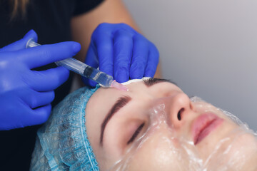 the cosmetologist makes an injection of mesotherapy preparation into the skin of the face.