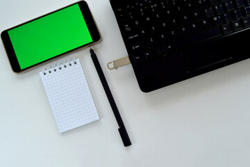 Smartphone green screen mockup and black pen with notepad. Technology concept of notepad and pen, laptop and flash drive