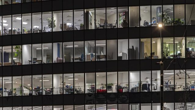 Office workers, during operation and at the end of the working day, visible through the windows of the business center, time lapse