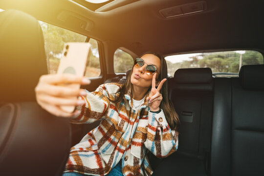 Stylish young woman sitting on back seat in the car and making selfie with smartphone. Woman taking picture with phone while sitting in taxi