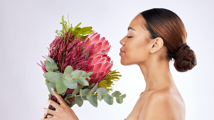 Stop and smell the flowers. Shot of a young woman smelling a bouquet of flowers against a studio background. - obrazy, fototapety, plakaty
