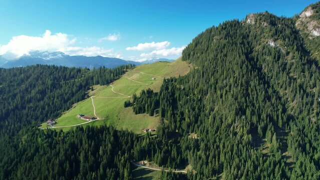 Drone shot of an alpine mountain landscape and a farm with alp meadows and a dirt road that leads up the mountain. Country life in Tyrol, Austria.