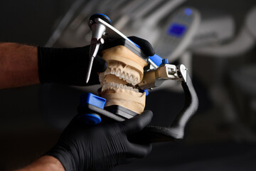 Dental technician or orthopedic dentist holding an articulator in the dental office. Dentist hands. The work of a technician in a dental laboratory. The concept of prosthetics and implantology.
