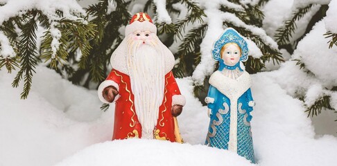 Christmas decorations (Russian Santa Claus and Snow Maiden) standing under the snowy Christmas tree. New Year, holiday background.	Banner.