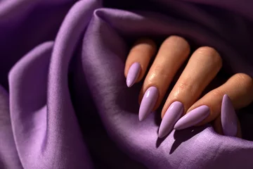 Tuinposter Girl's hand with an elegant manicure in a purple color on a purple silk background © nika57