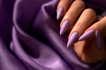 Girl's hand with an elegant manicure in a purple color on a purple silk background