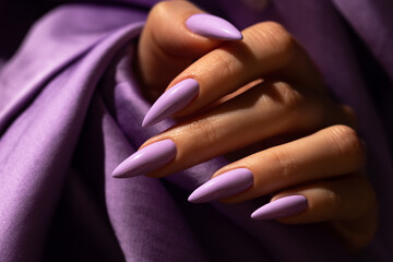 Girl's hand with an elegant manicure in a purple color on a purple silk background