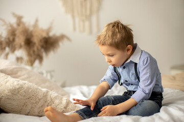 Fototapeta premium Beautiful fashion preschool child, boy, having fun at home in bed, looking out of the window