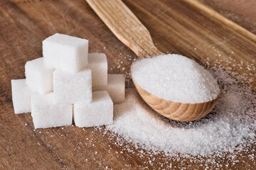 Fototapeta na wymiar Granulated sugar in wooden spoon and sugar cubes stacked in pyramid on wooden background.