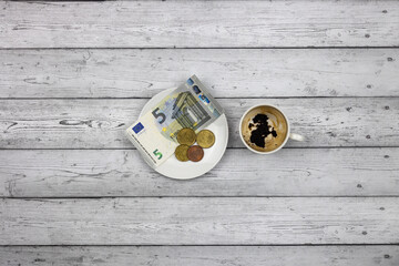 An empty cup and payment for coffee, a 5 euro bill and coins on a wooden table, top view