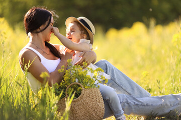 Mother and little daughter having fun in summer meadow with yellow flowers. Happy family on summer....