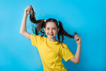 Fototapeta premium Little cute girl with a cute expression, posing in a yellow t-shirt on a blue bright background, emotional, funny