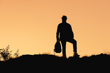 Fototapeta na wymiar the silhouette of man standing with bag in hat