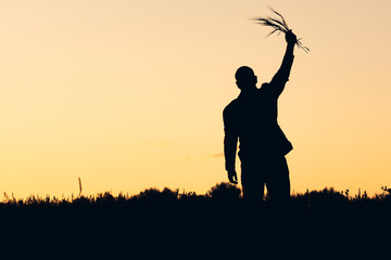 silhouette of a man raising spikelets of rye in his hand against the backdrop of sunset. the...