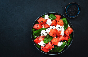 Summer Watermelon juicy salad bowl with feta cheese, spinach and black sesame seed, dark table...