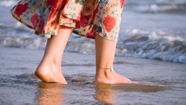 Close up shot of ocean waves washing over feet of young female. People enjoying summer vacation at tropical beach. Girl standing on seashore and enjoying tides of sea on trip