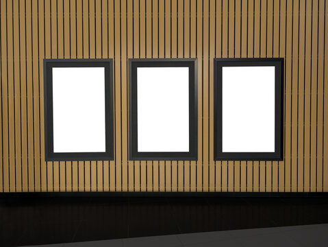 White template for three paintings, posters or photographs in an a black frame hung on a brown wooden wall, copy space